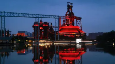 A circular industrial structure glows red beside still water at dusk.